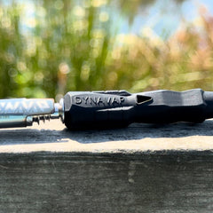 DynaVap B2 vaporizer with silicone stem and stainless steel cap resting outdoors on a wooden surface with blurred background.