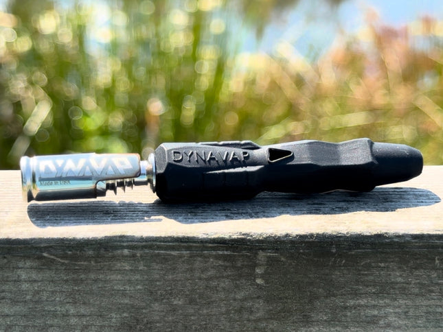 DynaVap B2 vaporizer with silicone stem and stainless steel cap resting outdoors on a wooden surface with blurred background.