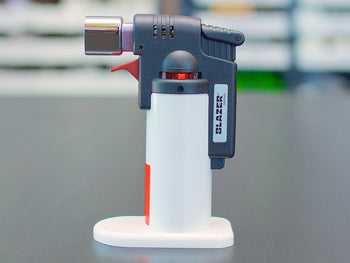 White Blazer Firefox Butane Torch lighter standing on a table.