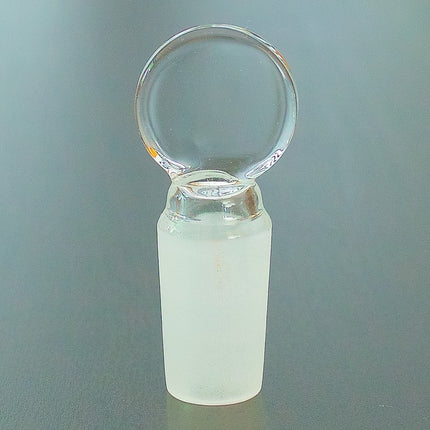 Flat top 14mm glass stopper on a table.