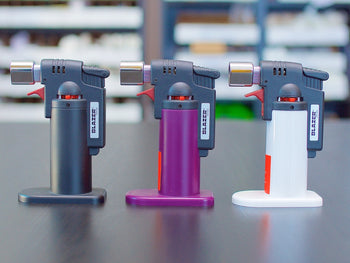 Black, purple and white Blazer Firefox Butane Torch lighters standing on a table.